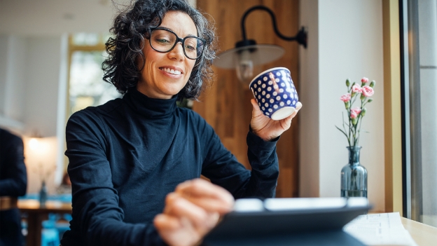 Lockige Frau mit schwarzer Brille und Tasse in der Hand